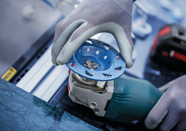 안전 장비를 착용한 사람이 전동 공구에 연삭 디스크를 부착합니다.