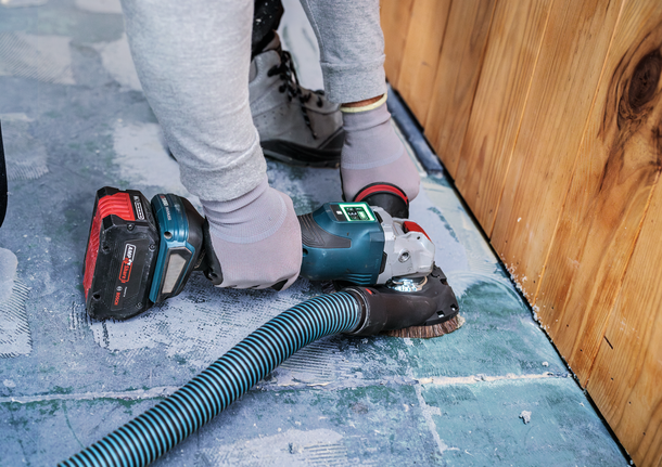 안전장비를 착용한 사람이 나무 벽 근처의 콘크리트 바닥을 샌딩하고 있습니다.