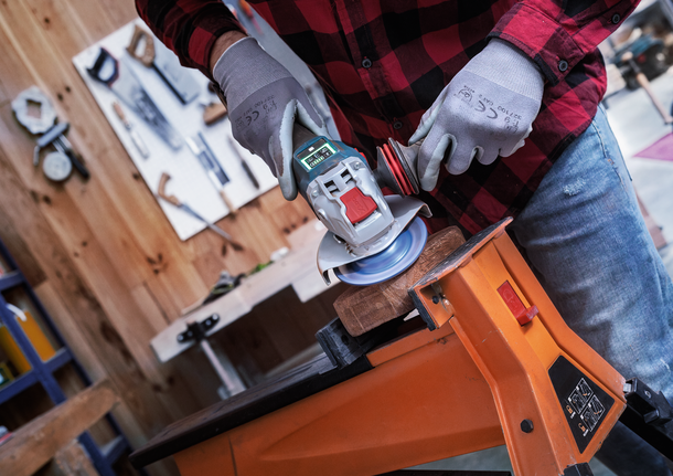 안전 장비를 착용한 사람이 각도 그라인더를 사용하여 작업대에 고정된 목재를 사포질하고 있습니다.