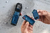 한 사람이 먼지 낀 콘크리트 바닥 위에 있는 도구 옆에 있는 파란색 배터리 칸을 엽니다.