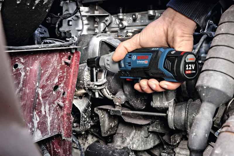 한 사람이 무선 래칫 렌치를 사용하여 엔진실의 볼트를 조입니다.