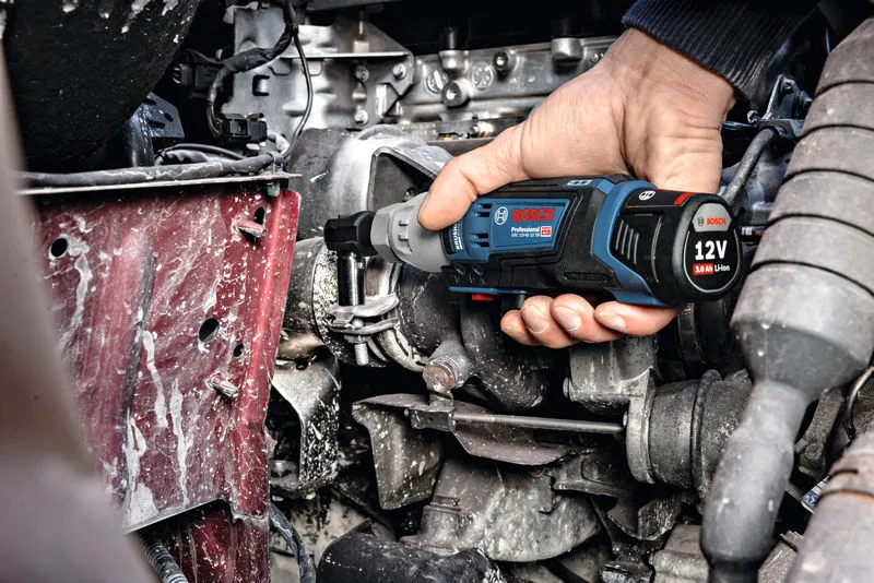 한 사람이 무선 래칫 렌치를 사용하여 엔진의 볼트를 조입니다.