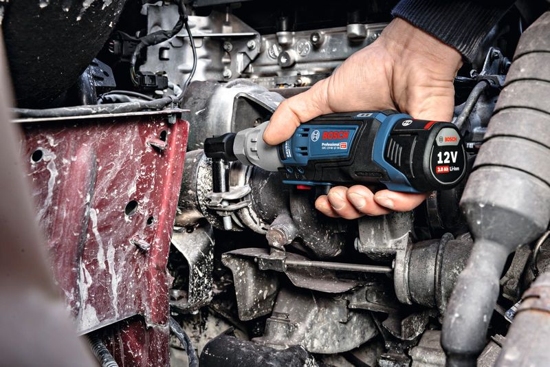 한 사람이 무선 래칫 렌치를 사용하여 엔진의 볼트를 조입니다.