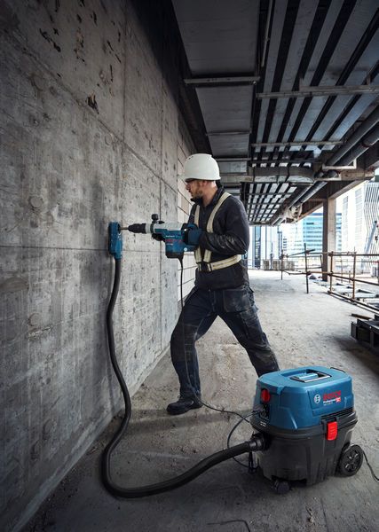 안전 장비를 착용한 사람이 습식 및 건식 추출기를 사용하여 콘크리트 벽에 구멍을 뚫고 있습니다.