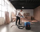 안전 장비를 착용한 사람이 목공 작업장에서 습식 건식 추출기를 사용하고 있습니다.