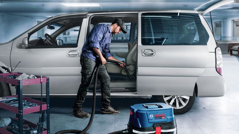 안전 장비를 착용한 사람이 습식 및 건식 추출기를 사용하여 자동차 내부를 청소하고 있습니다.