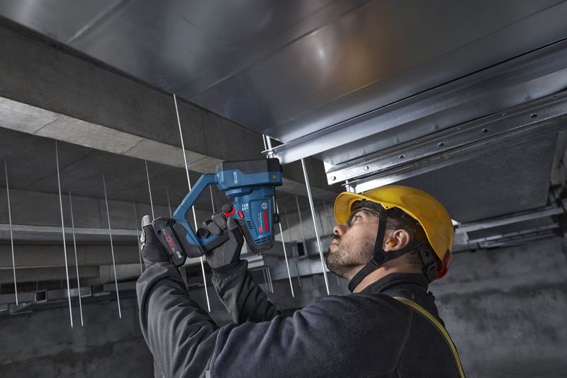 안전 장비를 착용한 사람이 무선 나사봉 커터를 천장 봉에 사용하고 있습니다.