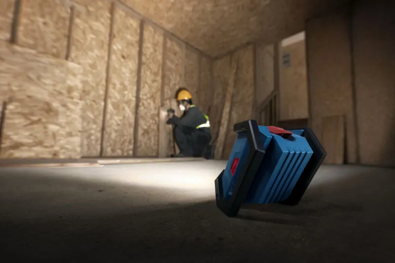 안전 장비를 착용한 사람이 무선 작업 현장 조명으로 조명을 비춰 건식벽체를 설치하고 있습니다.