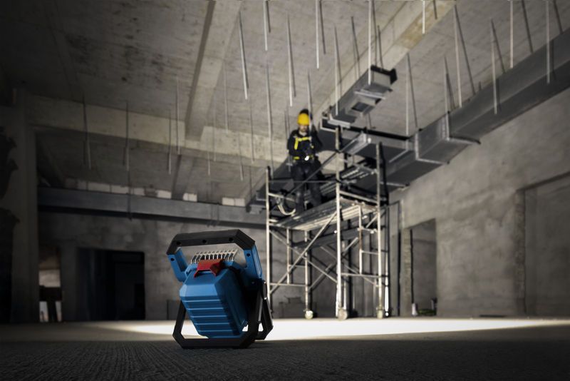 비계 위에서 안전 장비를 착용한 사람을 비추는 무선 작업 현장 조명입니다.