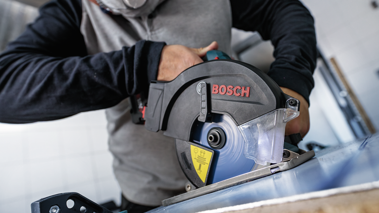 안전 장비를 착용한 사람이 원형 톱으로 금속판을 자릅니다.