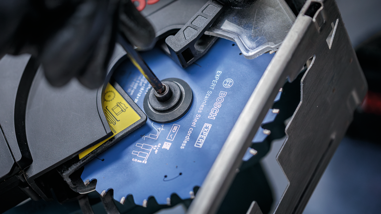 안전 장비를 착용한 사람이 손도구를 이용해 원형 톱날을 조이고 있습니다.