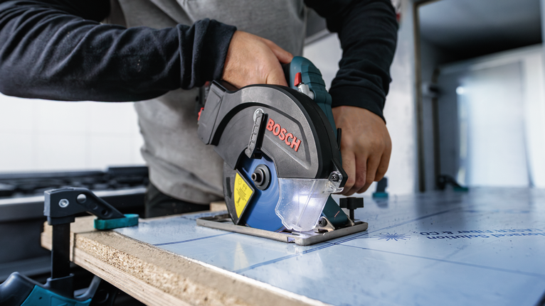 작업대에 고정된 보드를 자르기 위해 원형 톱을 조작하는 사람.