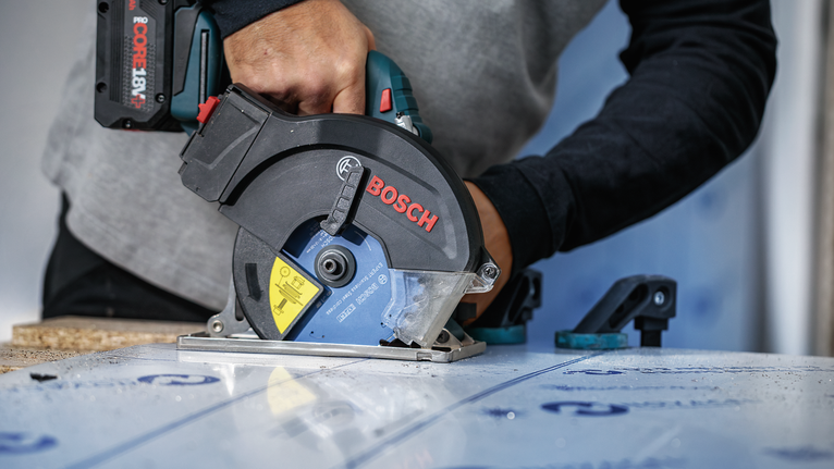 안전 장비를 착용한 사람이 원형 톱을 사용하여 적층판을 자릅니다.