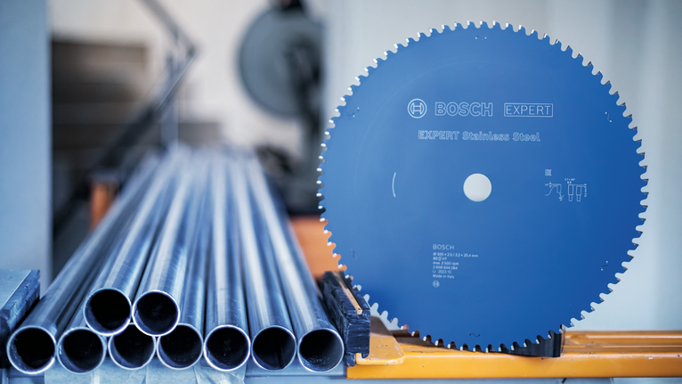 산업용 작업대에 쌓여 있는 금속 파이프 옆에 원형 톱날이 놓여 있습니다.