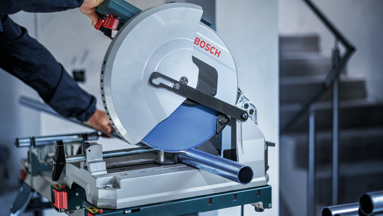 안전 장비를 착용한 사람이 원형 톱으로 금속 파이프를 자릅니다.