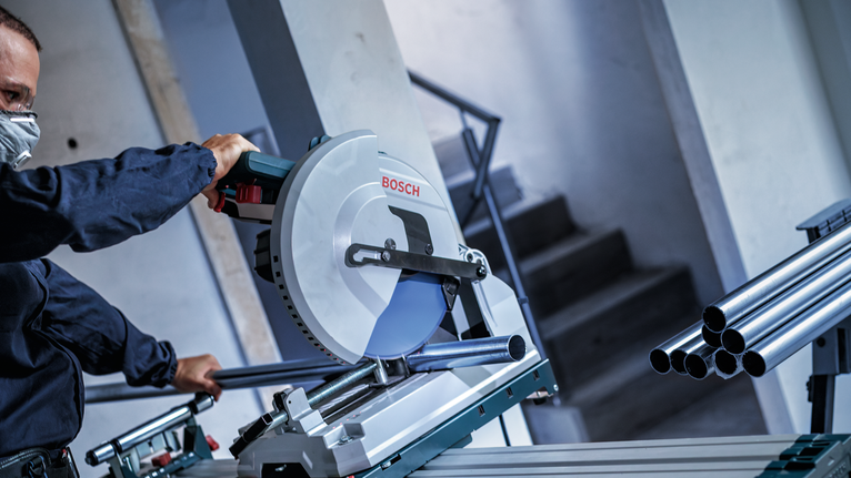 안전 장비를 착용한 사람이 원형 톱으로 금속 파이프를 절단하고 있습니다.