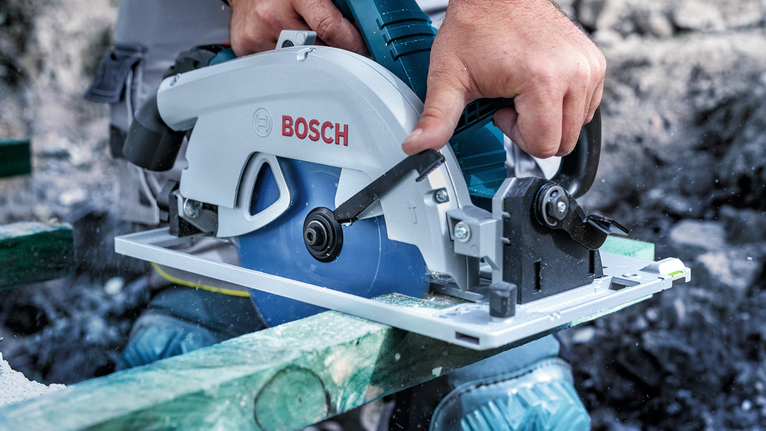 안전장비를 착용한 사람이 원형 톱으로 나무를 자릅니다.