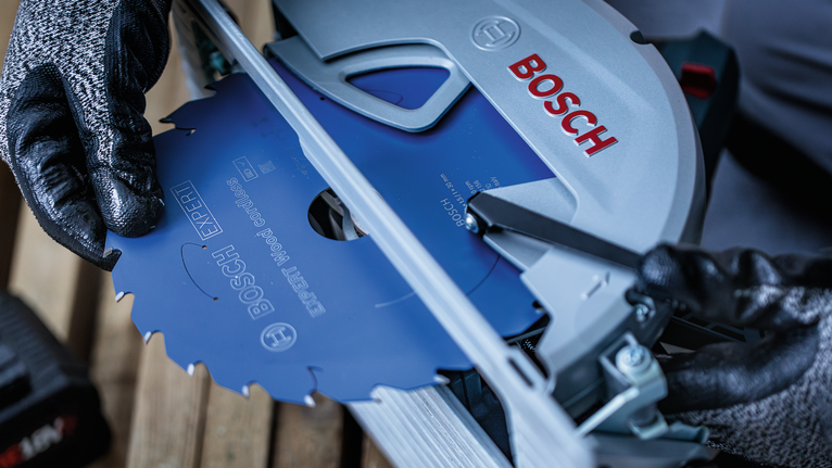 안전 장비를 착용한 사람이 전동 공구에 원형 톱날을 설치하고 있습니다.