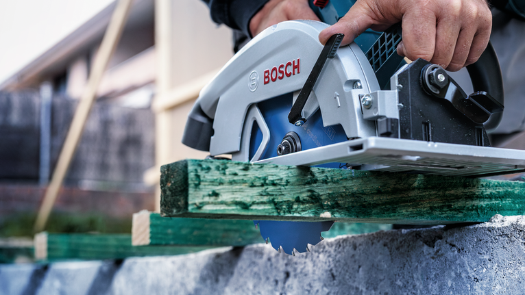 안전 장비를 착용한 사람이 원형 톱으로 생목을 자르고 있습니다.