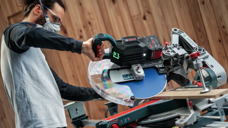 안전 장비를 착용한 사람이 작업장에서 원형 톱을 사용하여 나무를 자르고 있습니다.