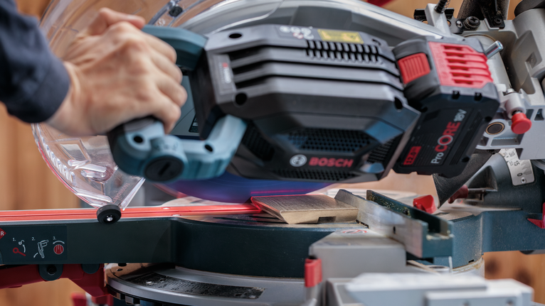 사람이 나무판 위로 슬라이딩 마이터 톱을 안내하고 있습니다.