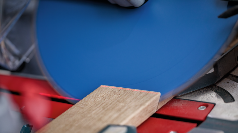 안전장비를 착용한 사람이 원형 톱으로 나무 판자를 자르고 있습니다.