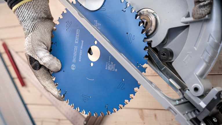 안전 장비를 착용한 사람이 마이터 톱에 원형 톱날을 설치하고 있습니다.