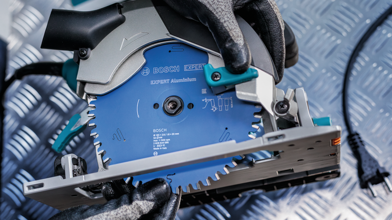 안전 장비를 착용한 사람이 금속 무늬 표면에서 원형 톱을 조정하고 있습니다.