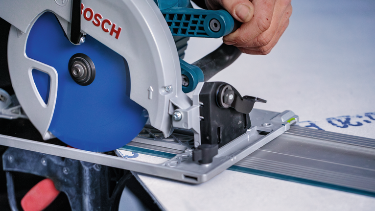 한 사람이 작업대 위의 직선 경로를 따라 파란색 톱날이 달린 원형 톱을 움직입니다.