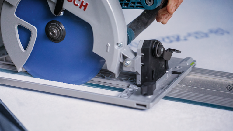 안전 장비를 착용한 사람이 원형 톱을 이용해 금속 트랙을 따라 건식벽체를 절단하고 있습니다.