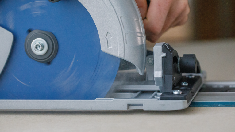 가이드 레일을 따라 나무를 자르기 위해 원형 톱을 조작하는 사람.