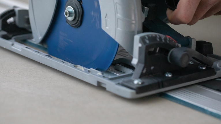 사람이 원형 톱을 금속 트랙을 따라 움직여 나무판을 자릅니다.