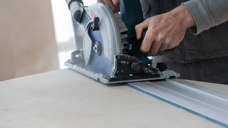 사람이 원형 톱을 궤도를 따라 움직여 큰 판자를 자릅니다.