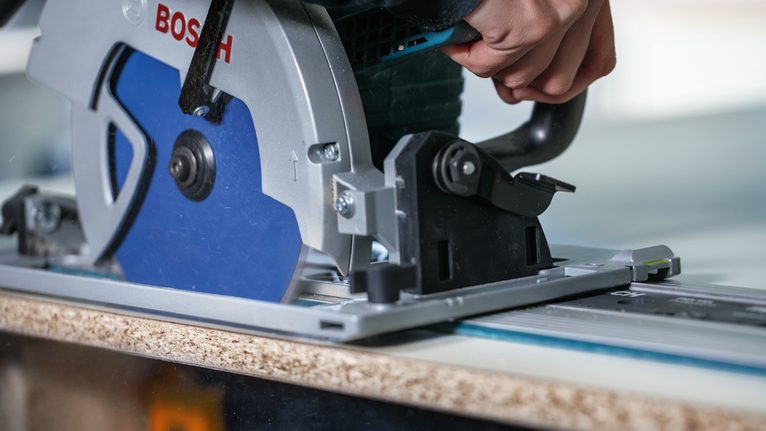 사람이 원형 톱을 궤도를 따라 움직여 나무판을 자릅니다.