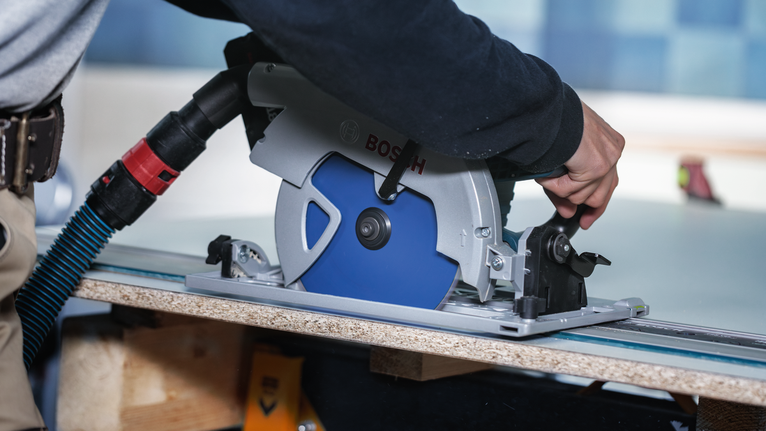 안전 장비를 착용한 사람이 나무판을 따라 원형 톱을 조정하고 있습니다.