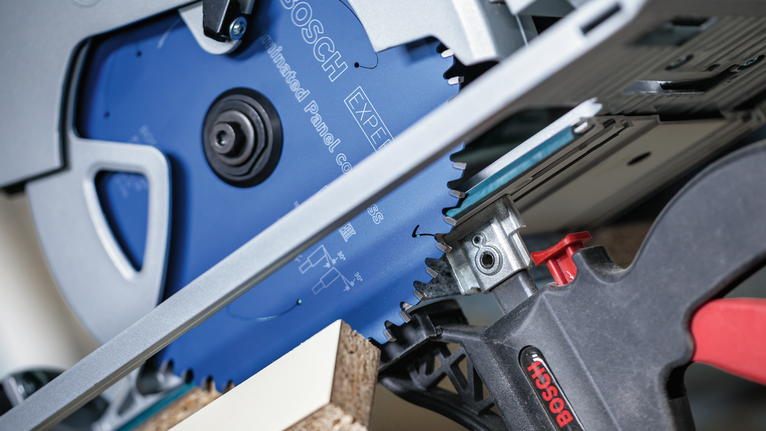 작업대에 고정된 파티클보드를 원형 톱으로 절단하는 모습입니다.