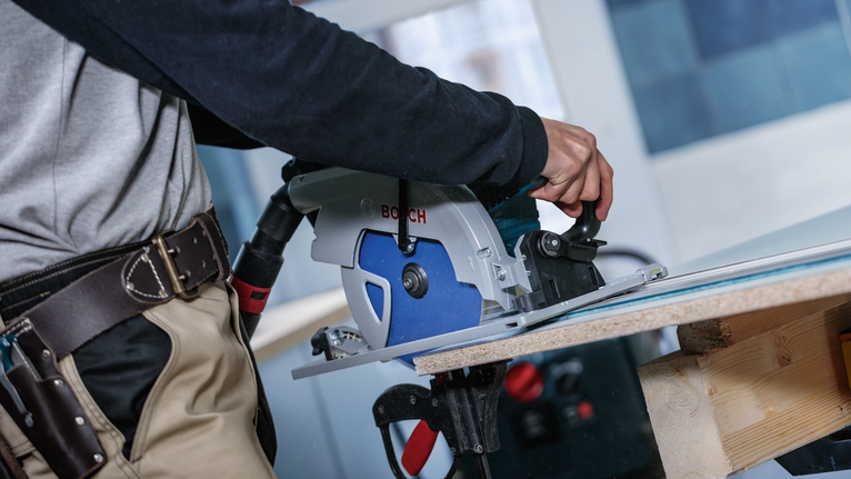 안전 장비를 착용한 사람이 원형 톱을 사용하여 나무판을 자르고 있습니다.