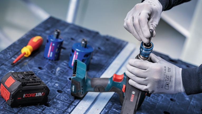 안전 장비를 착용한 사람이 무선 전동 공구에 드릴 비트를 부착하고 있습니다.