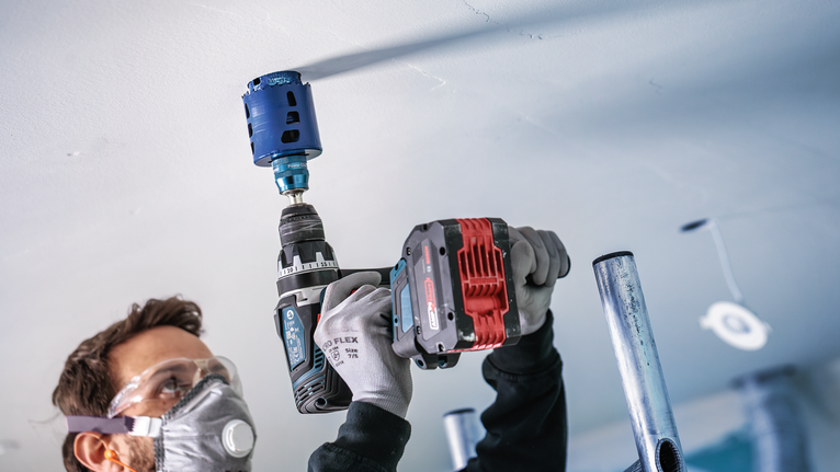 안전장비를 착용한 사람이 전동공구를 이용해 천장에 큰 구멍을 뚫고 있습니다.