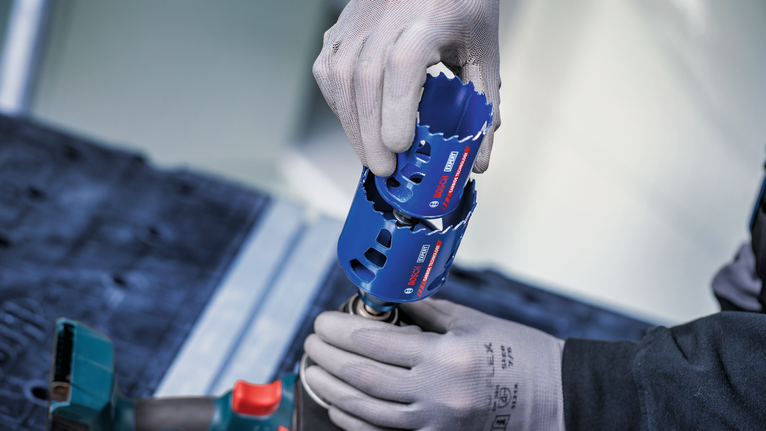 안전 장비를 착용한 사람이 전동 공구에 파란색 홀 톱을 부착하고 있습니다.