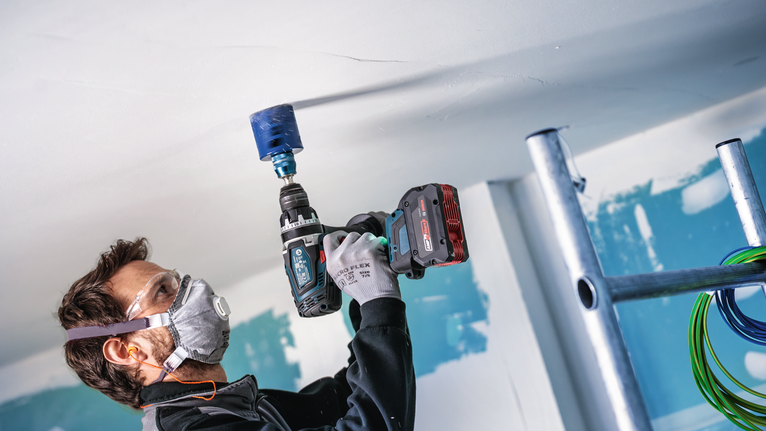 안전 장비를 착용한 사람이 건설 현장의 천장에 원형 구멍을 뚫고 있습니다.