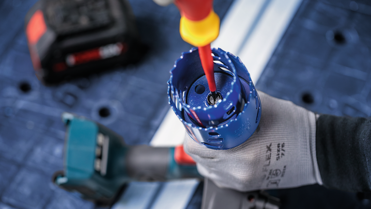 안전 장비를 착용한 사람이 전동 드릴에 부착된 홀 톱을 조정하고 있습니다.