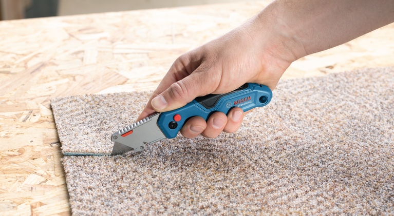 사람이 다용도 칼을 이용해 나무 표면의 카펫을 자릅니다.