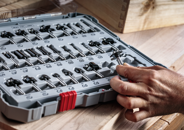 사람이 나무 작업대 위에 정리된 도구 세트에서 라우터 비트를 선택하고 있습니다.