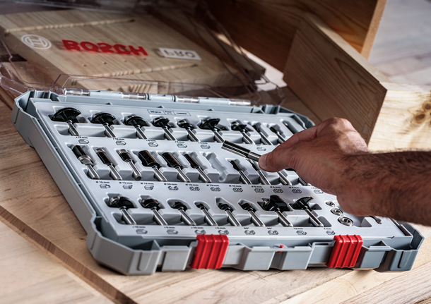 사람이 나무 테이블 위에 정리된 세트에서 드릴 비트를 선택합니다.