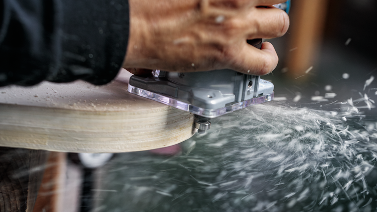 사람이 전동 공구를 나무 가장자리를 따라 움직이자 톱밥이 흩어진다.
