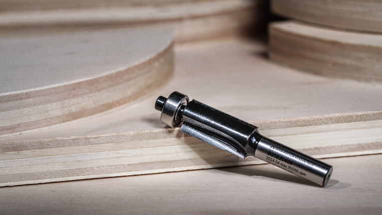 합판 시트가 쌓여 있는 곳 근처의 나무 표면에 라우터 비트를 놓은 모습입니다.