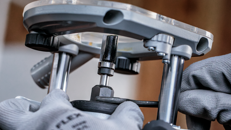 안전 장비를 착용한 사람이 금속 라우터 도구를 조정하고 있습니다.