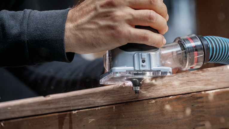 사람이 전동 라우터를 나무 판자 위로 움직여 정밀한 모서리 모양을 만듭니다.