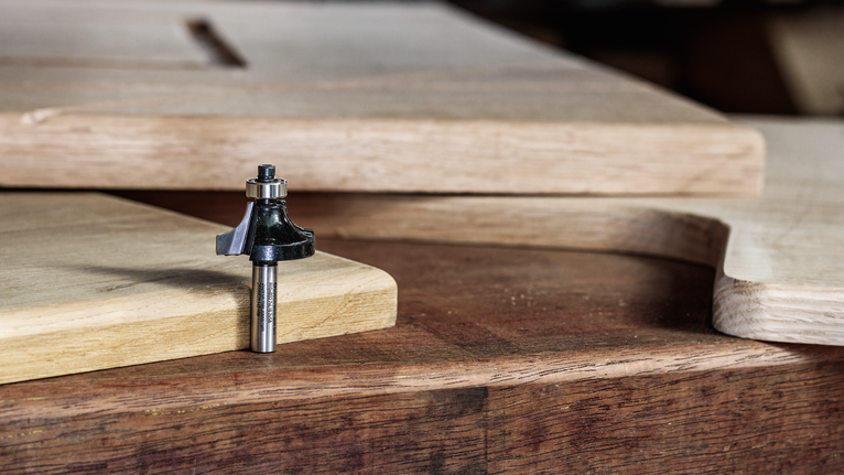 잘라서 모양을 만든 목재 패널 옆에 있는 나무 작업대 위에 라우터 비트를 올려놓은 모습입니다.